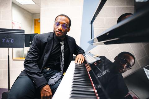 Loba Salami sits at a piano wearing a black suit and tie.